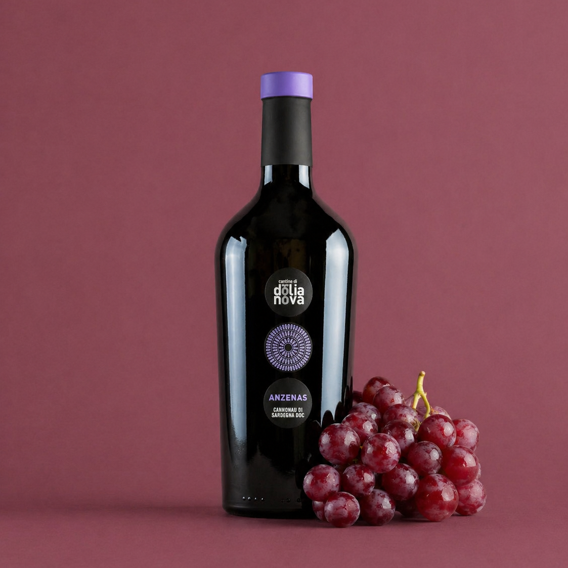 Anzenas Cannonau di Sardegna red wine bottle with red grapes on deep red background