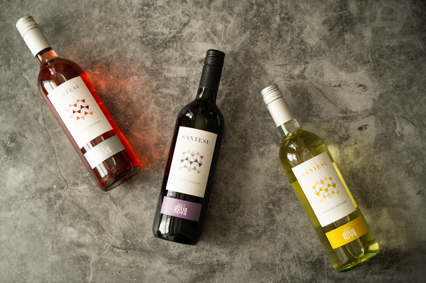 Santesu red, white and rosé Sardinian wine bottles on a textured stone background